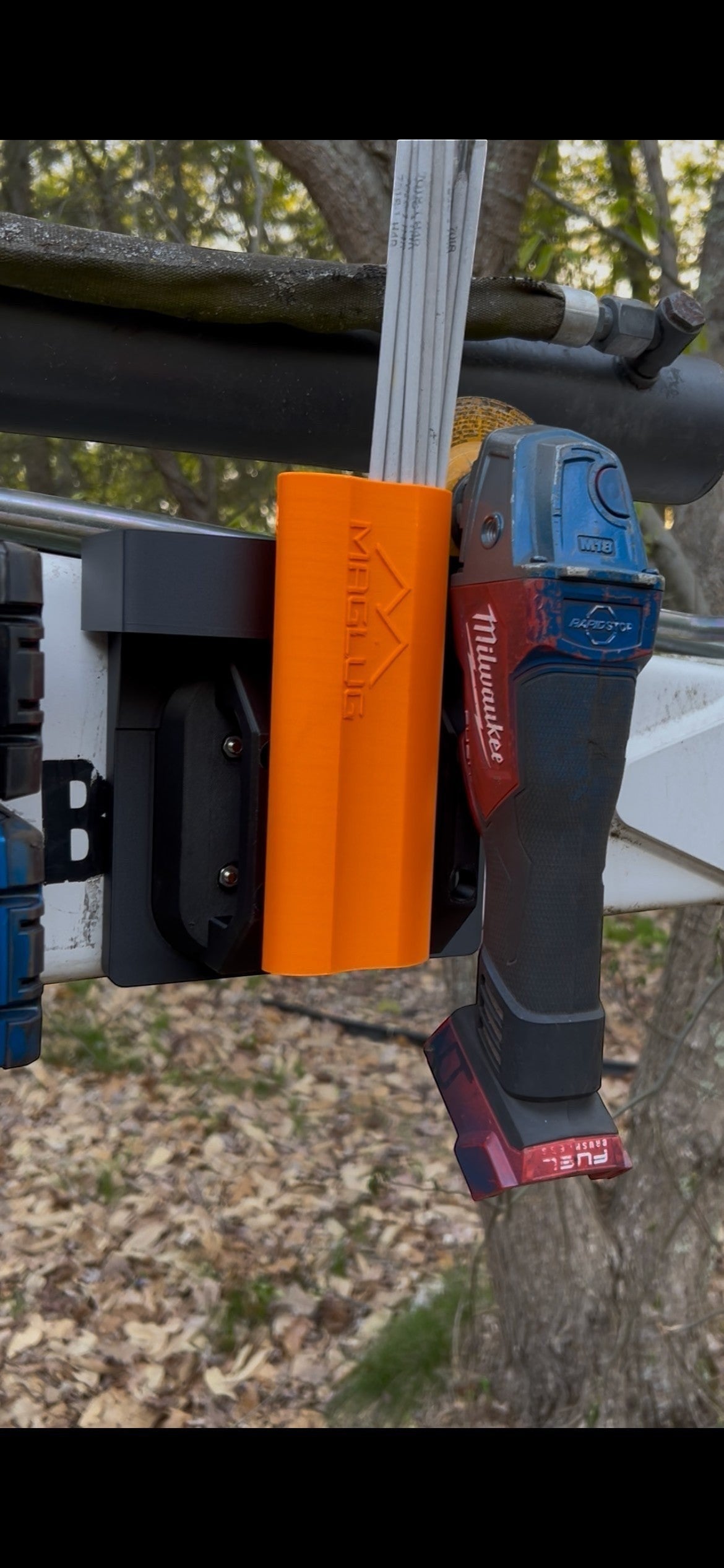 Cold Composites MagLug orange magnetic handle holding welding rods, with a Milwaukee grinder attached to a magnetic workstation.